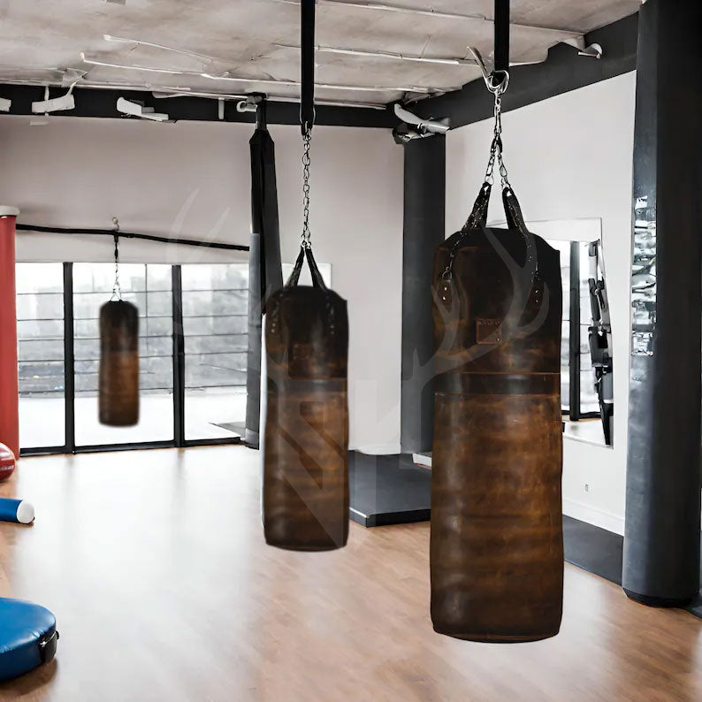 Legacy Striker cowhide leather punching bag hanging in a rustic gym setup. The bag showcases handcrafted leather texture, detailed reinforced stitching, and heavy-duty steel chains. Ideal for boxing and MMA, this professional-grade heavy bag is built from premium leather for durability, making it perfect for intense combat training, footwork drills, and powerful strikes.