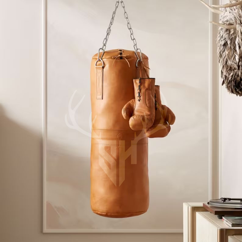 Sundown Tan Leather Heavy Punching Bag hanging in a gym setting. Made with premium full-grain cowhide leather, reinforced stitching, and a stainless steel hanging chain. Unfilled for custom weight, ideal for boxing, MMA, Muay Thai, and home gym workouts. The natural tan finish adds a vintage, stylish look.