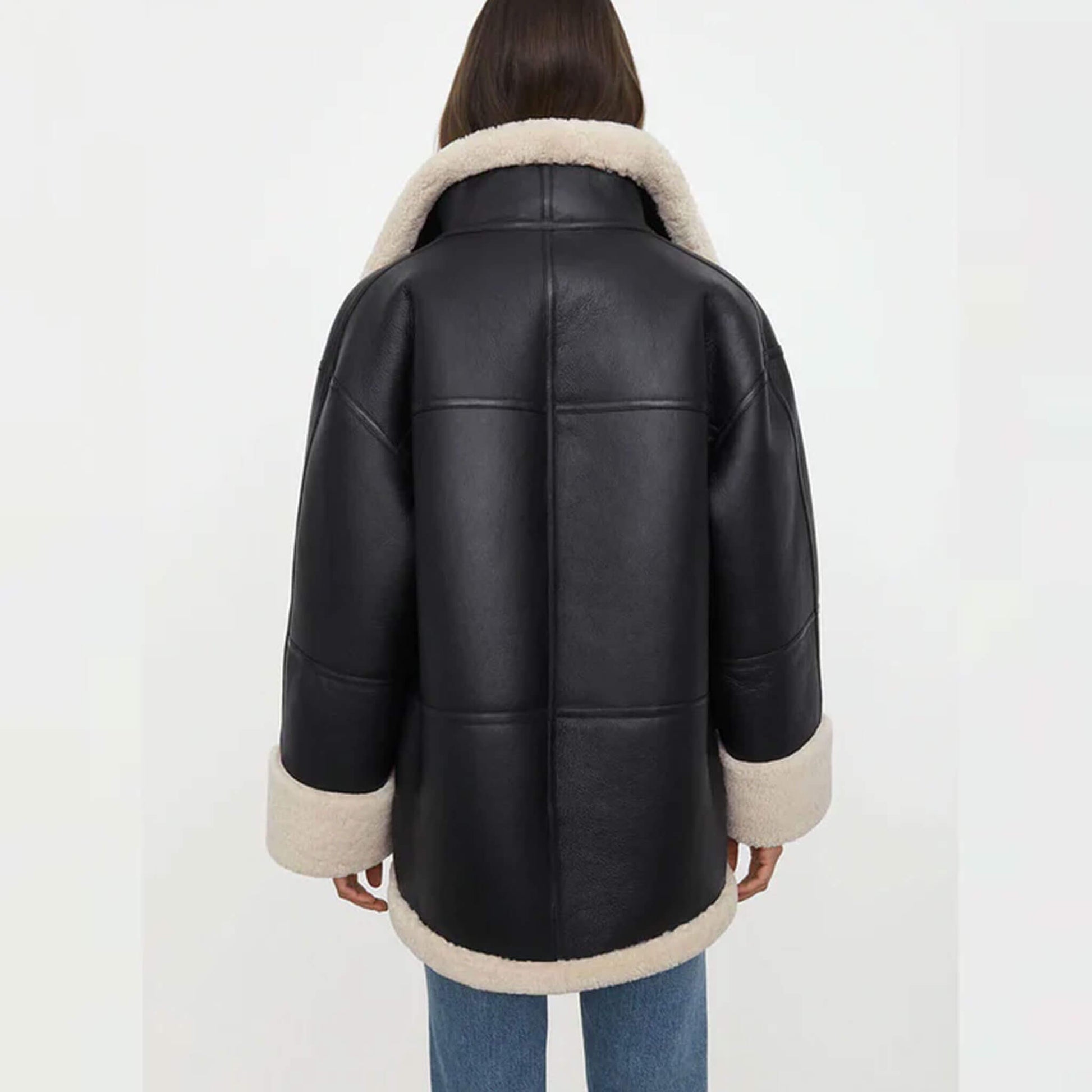 Back view of a women’s oversized black shearling jacket made from goatskin leather with faux fur lining. The oversized cut drapes naturally, with cream shearling accents along the hem, collar, and cuffs. This relaxed-fit shearling coat is designed for warmth and style, making it an essential oversized winter leather jacket for women who value comfort and timeless fashion.