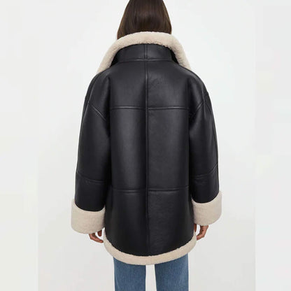 Back view of a women’s oversized black shearling jacket made from goatskin leather with faux fur lining. The oversized cut drapes naturally, with cream shearling accents along the hem, collar, and cuffs. This relaxed-fit shearling coat is designed for warmth and style, making it an essential oversized winter leather jacket for women who value comfort and timeless fashion.