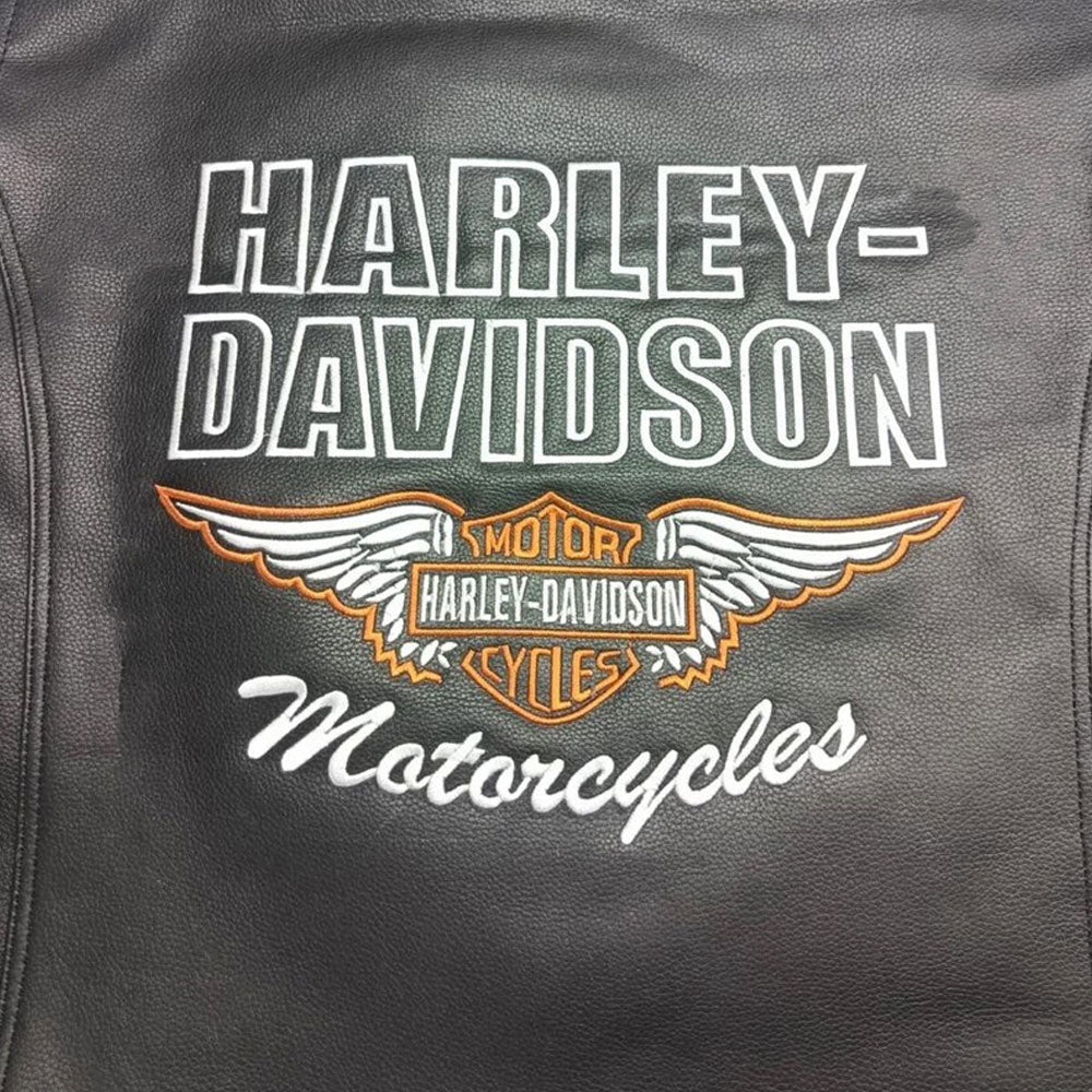 Detailed close-up of the Harley-Davidson embroidered logo on the black cowhide café racer vest. Showcases fine stitching, authentic branding, and the premium craftsmanship that makes this vest a standout choice for bikers and Harley fans alike.

